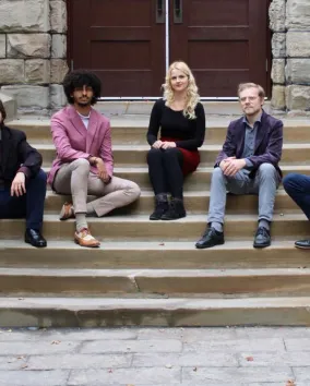 Diapente Renaissance Vocal Quintet Five young people sit facing the camera on the stone steps of a historic building.
