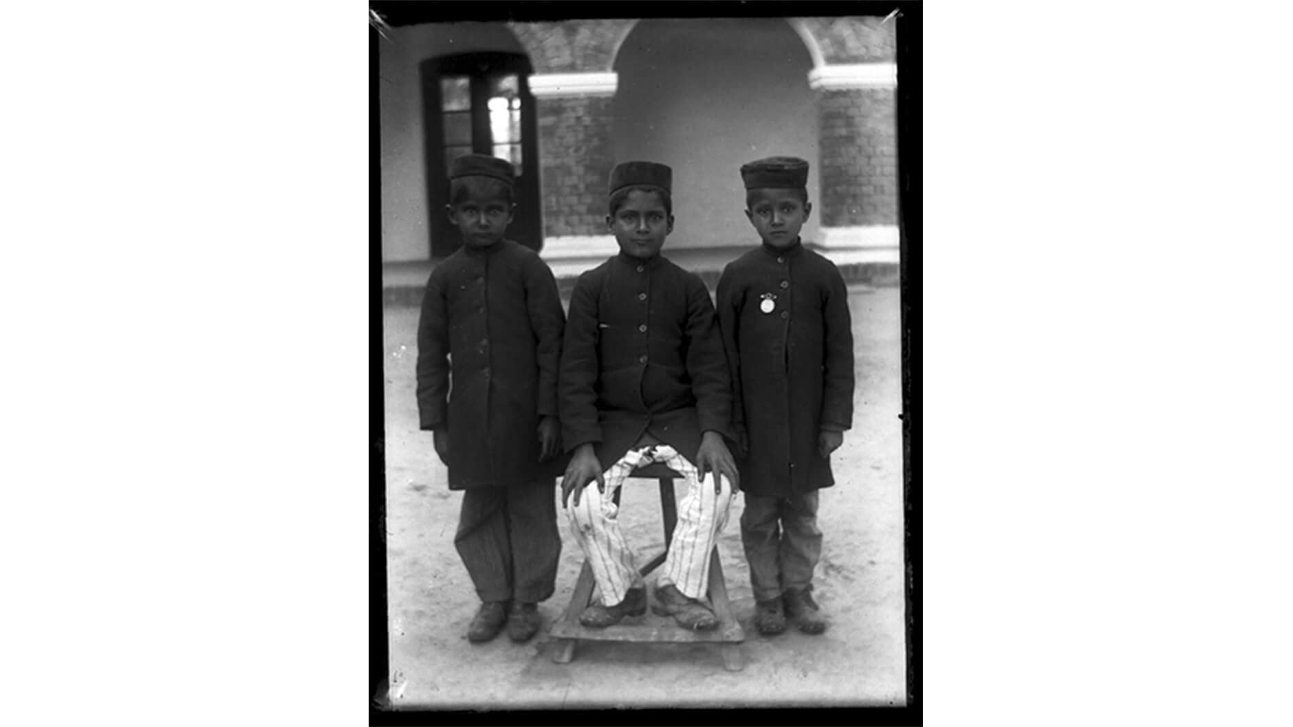 Portrait de trois garçons vêtus de vestes et de chapeaux sombres.