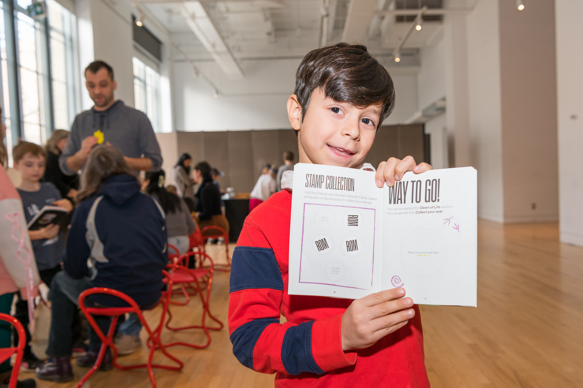 A boy excitedly holds an open activity book showing his stamps and stickers.