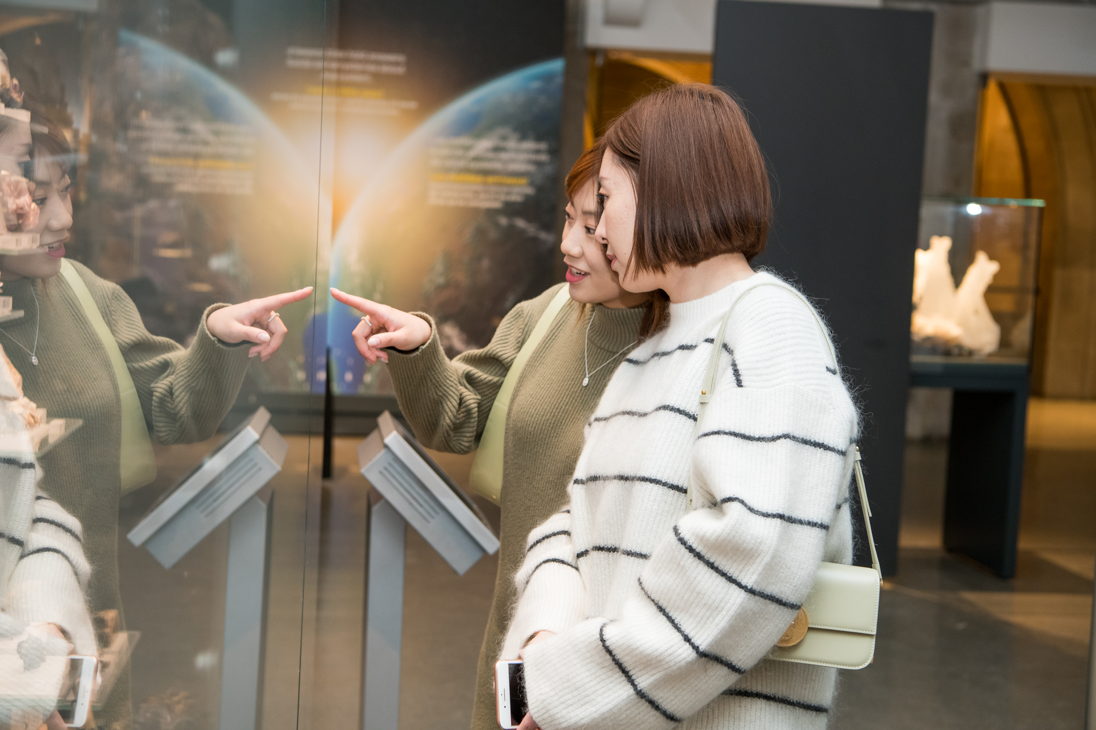 A woman points out a gem she is looking at to her friend. She is looking at the unseen gem with a sense of with wonder.