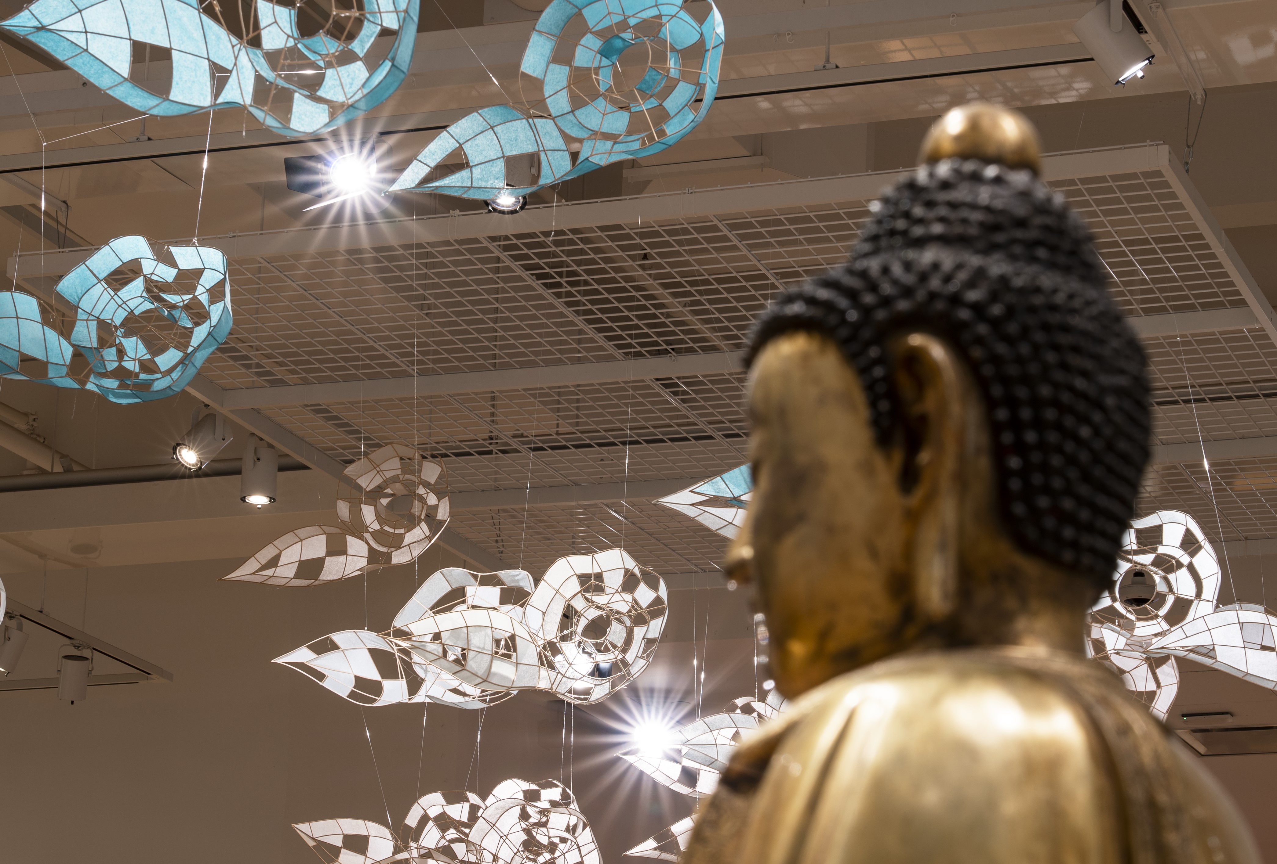 Des nuages en papier flottent dans le ciel au-dessus de la tête d'une buddah en bronze. 