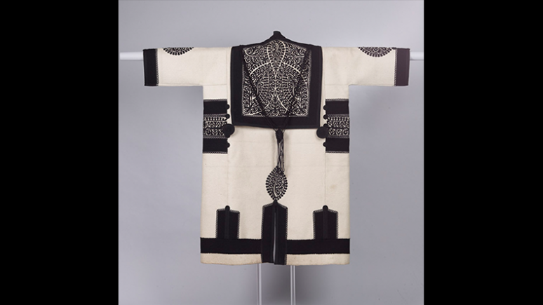 Szür (manteau) d'homme. Fabriqué dans l'actuelle Roumanie selon la tradition hongroise de Transylvanie. Vers 1900. Étoffe de laine blanche pleine, garnie de bandes appliquées de tissu noir et de motifs découpés en feutre noir ; garniture enrichie de petits ronds noirs noués. 970.227.9 Don de la Société hongroise Helikon, 1973.