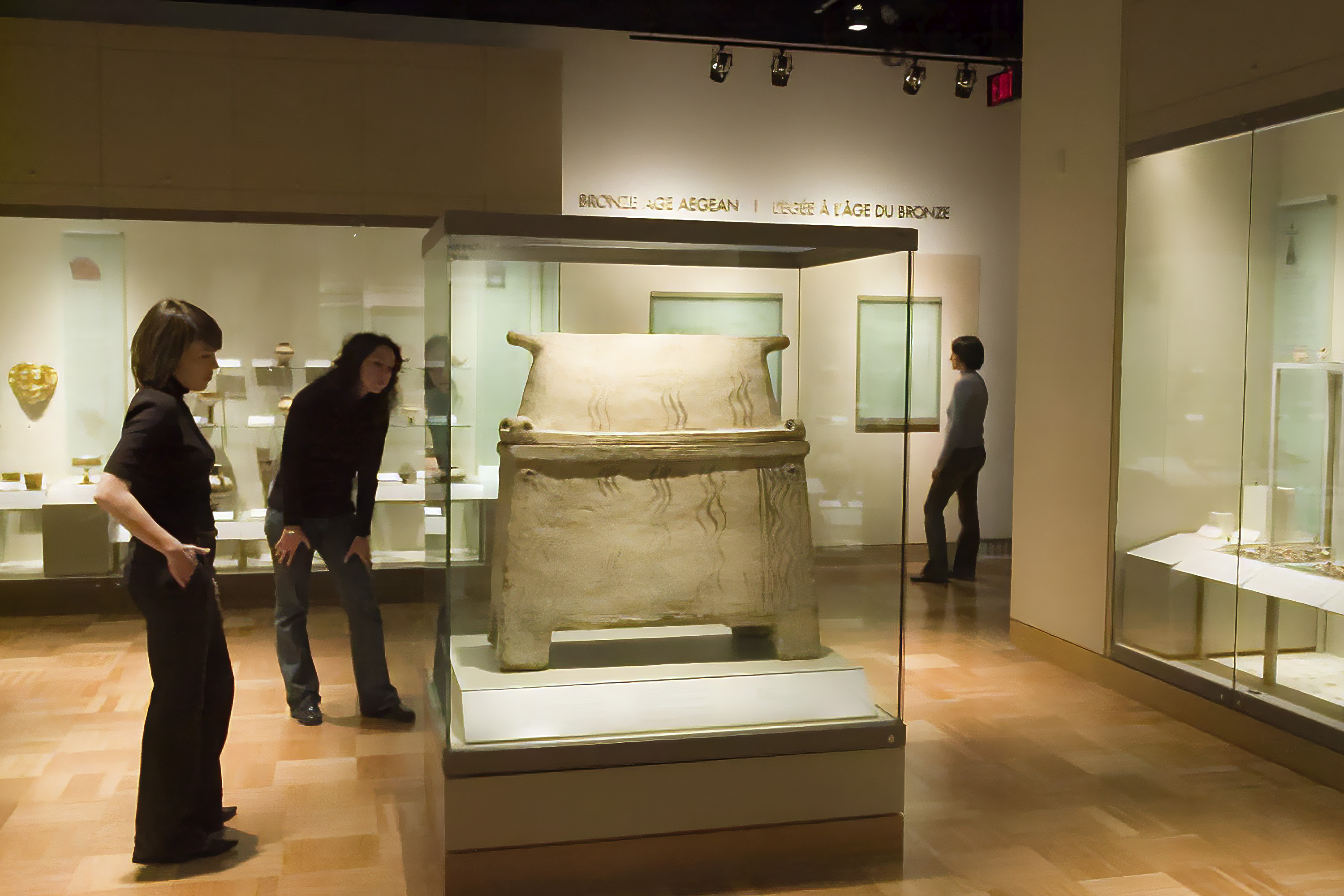 Two people examine a sarcophagus in a gallery, one leans forward to get a closer look at the details.