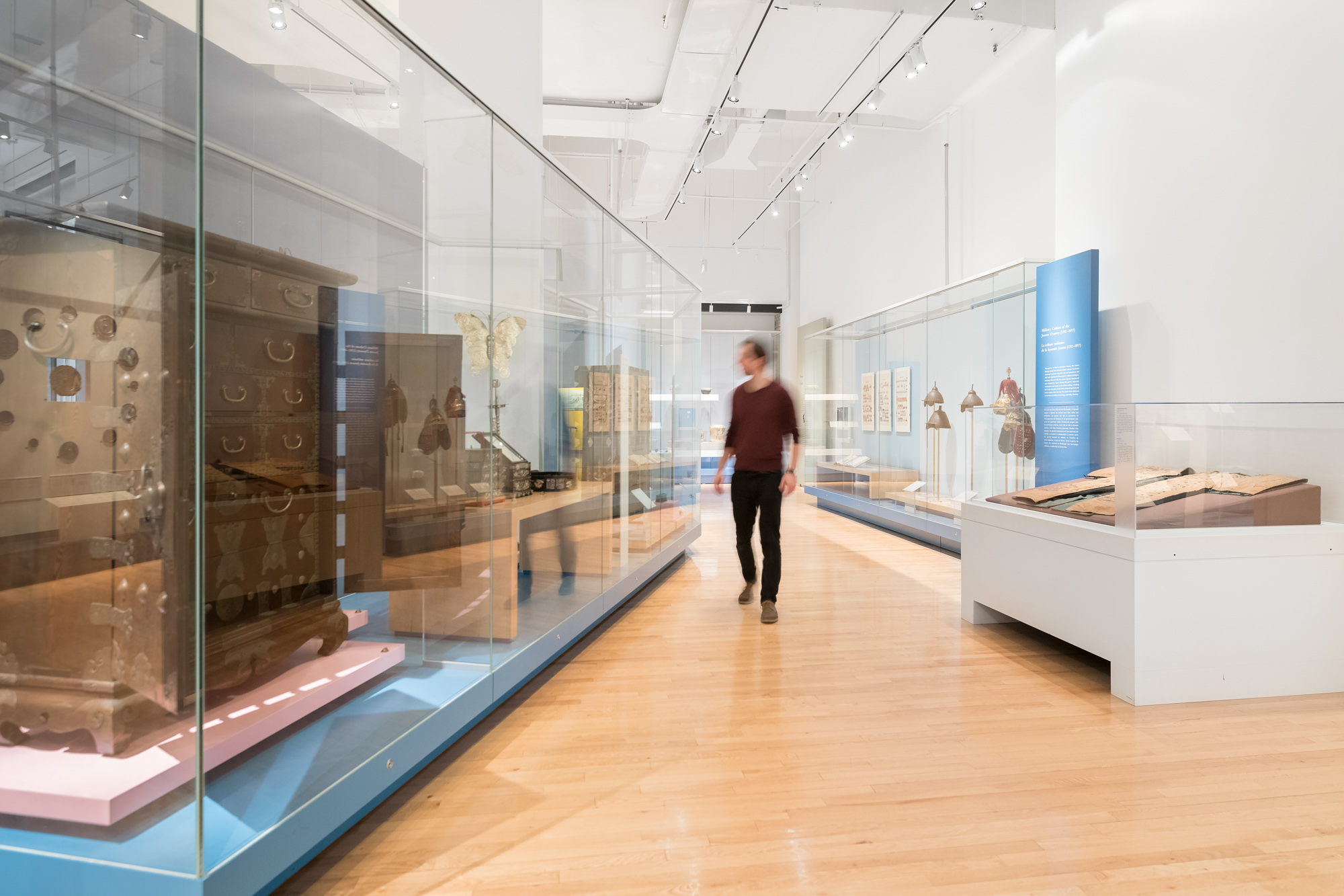 A person walks through a gallery admiring the large furniture in glass cases/