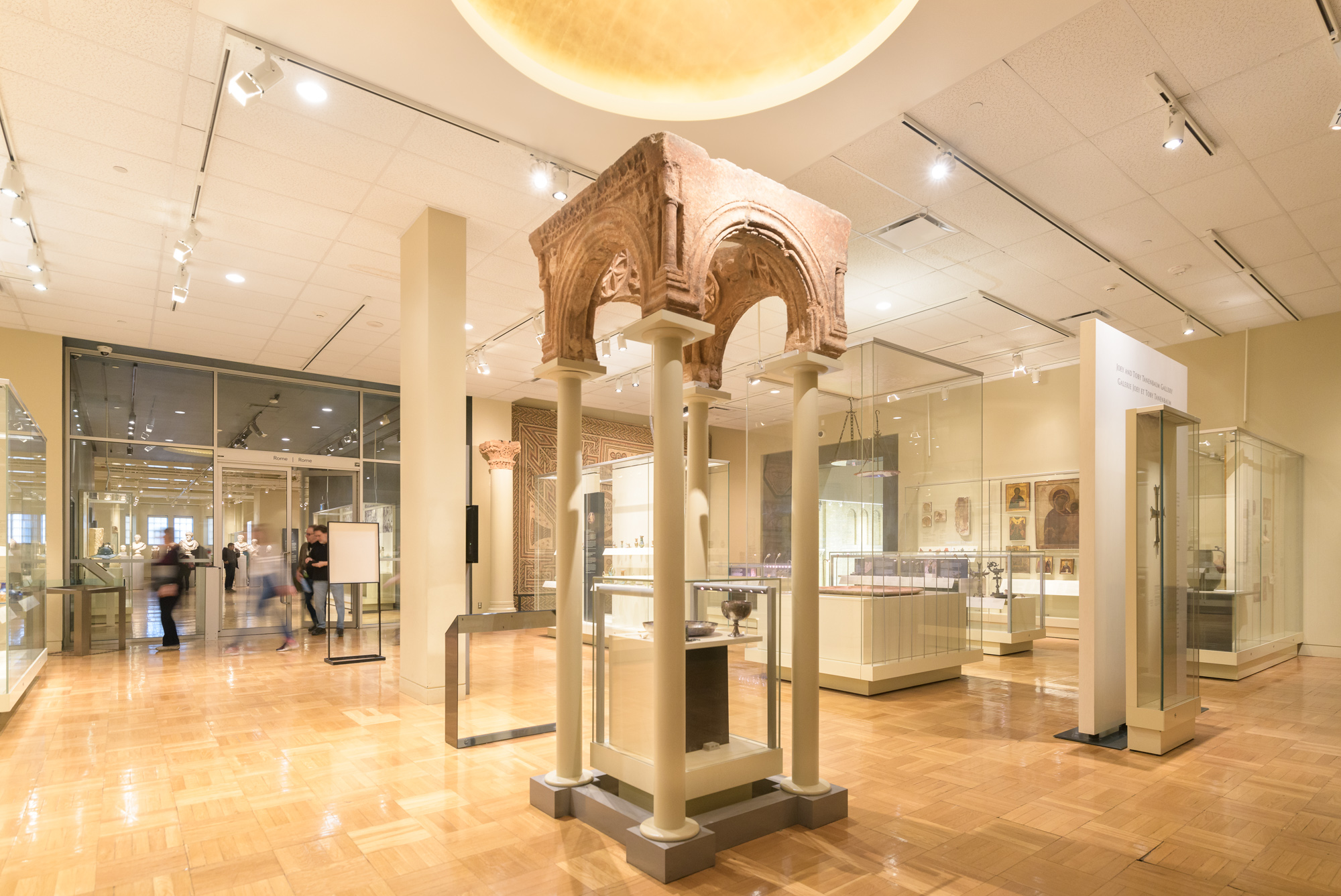 An ancient archway supported by modern pillars above a case containing a goblet and bowl.