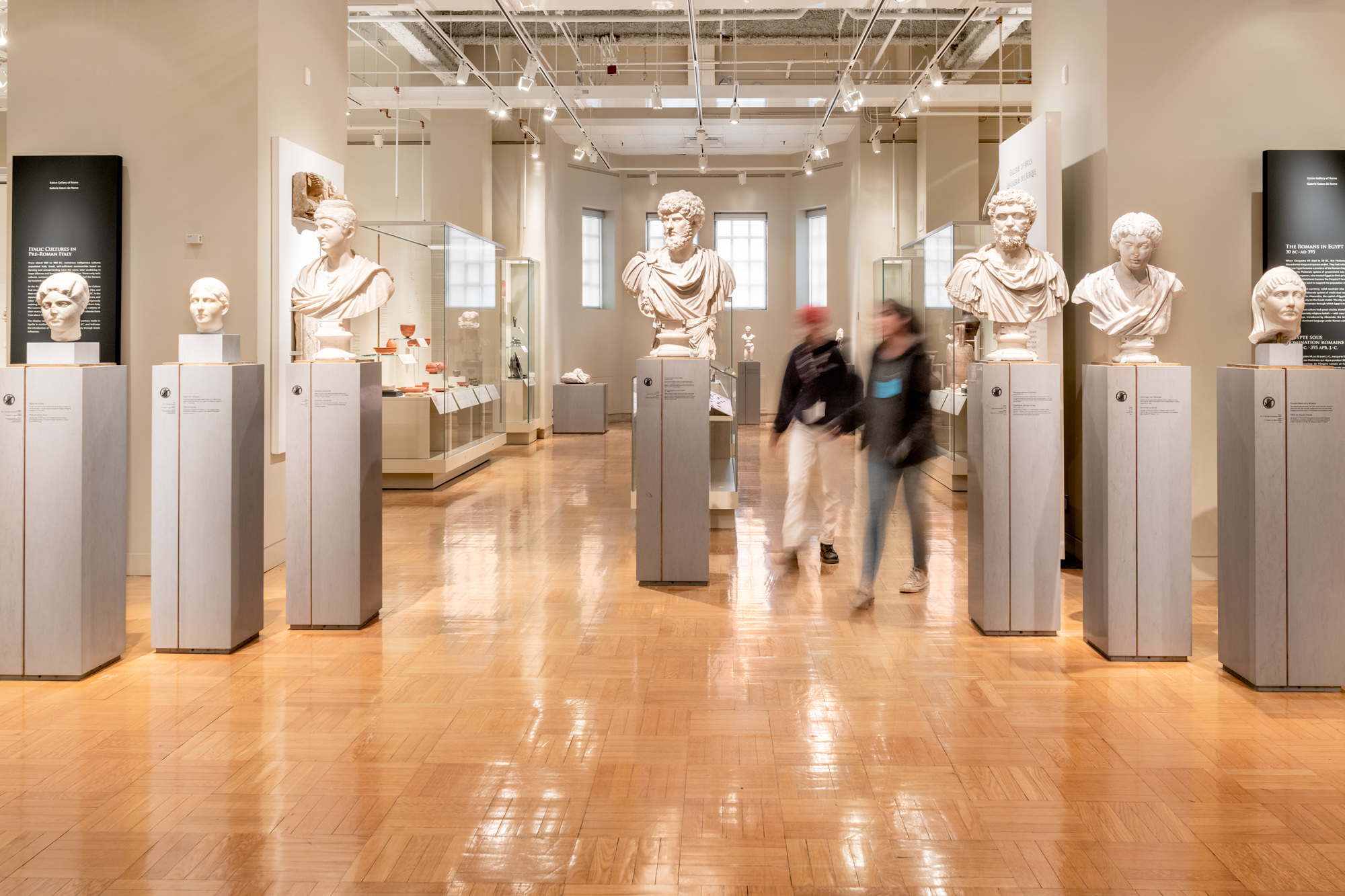 Two people walk among the marble busts of important Romans.