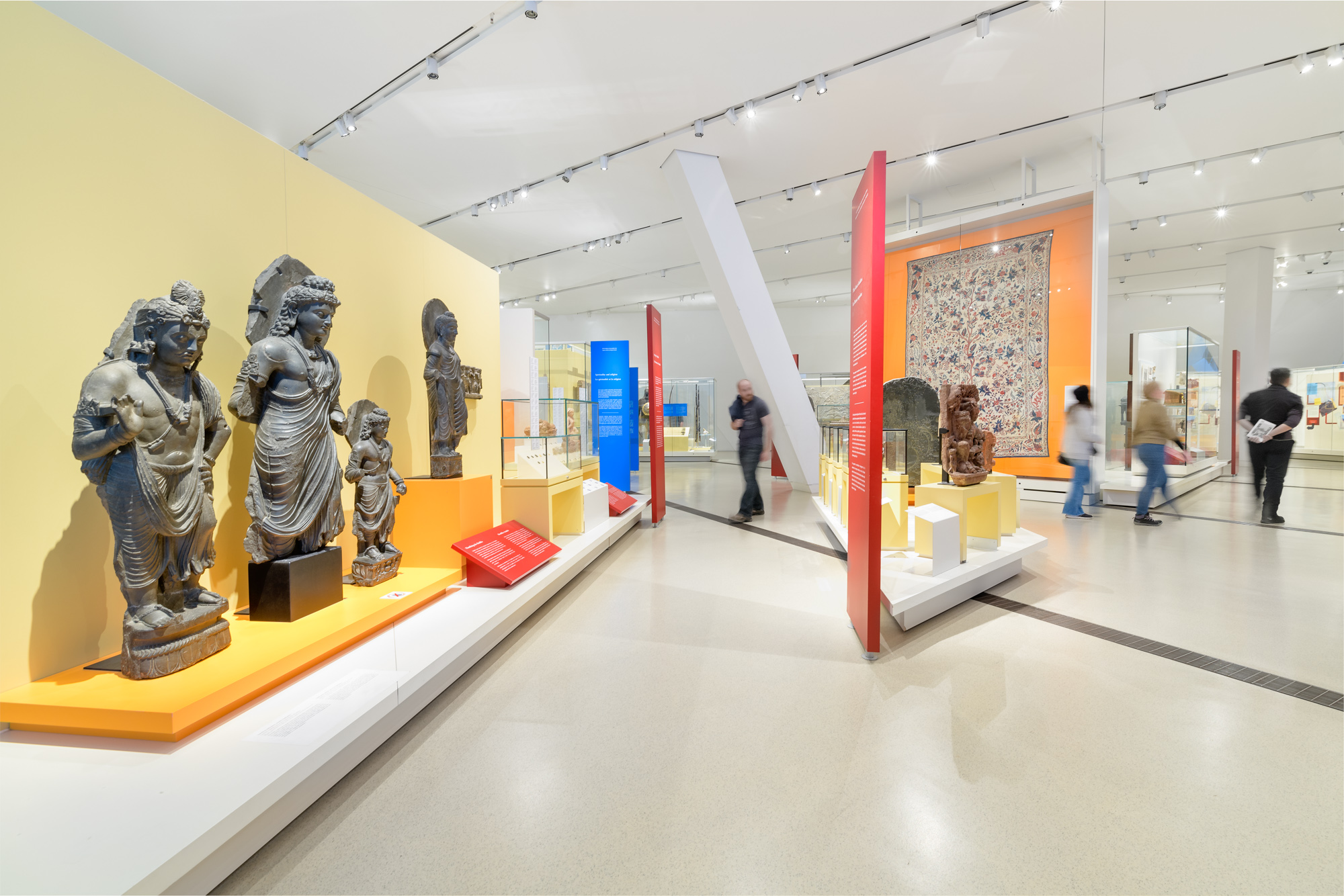 People walk around a gallery featuring statues of South Asian religious figures.