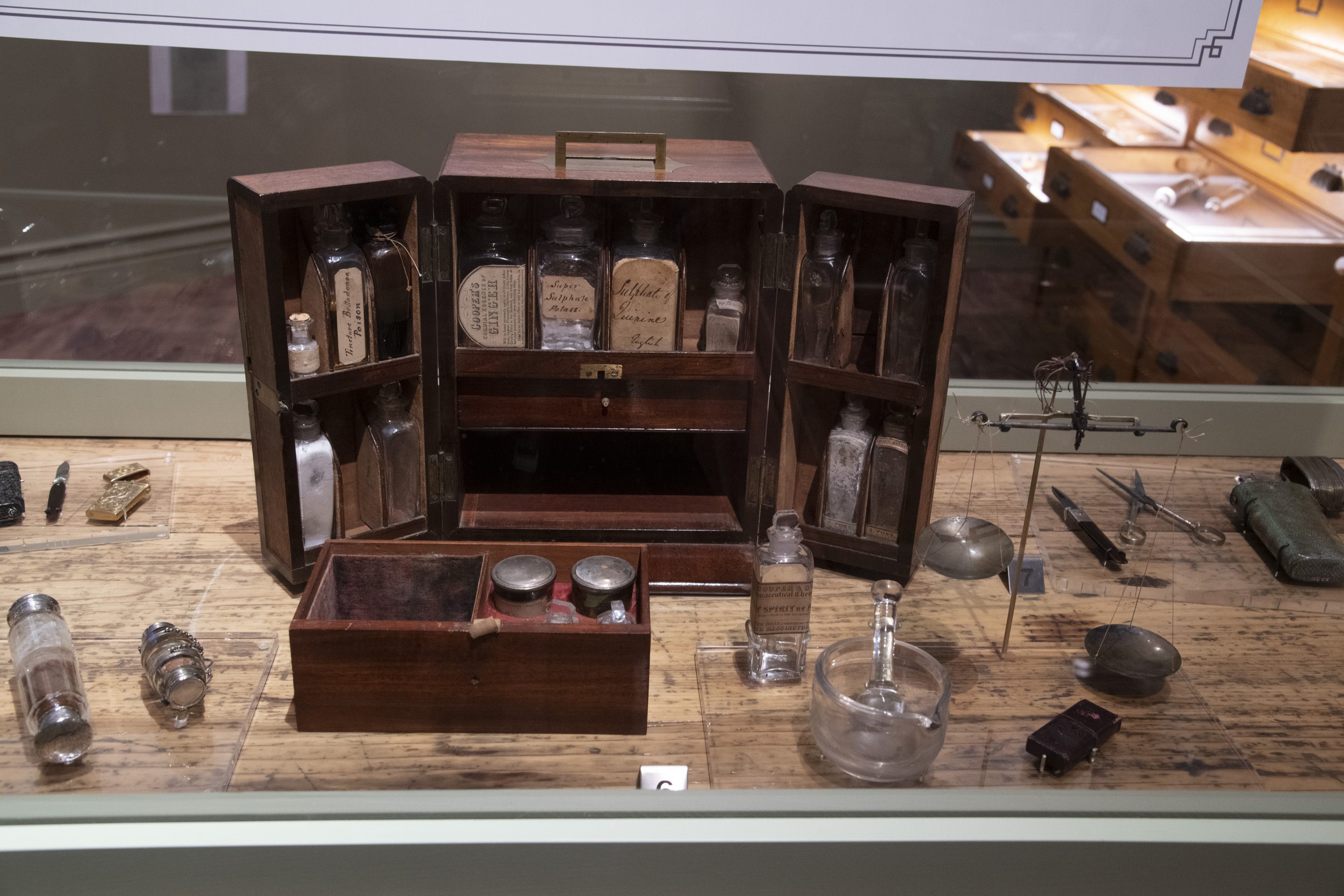 A vintage wooden apothecary box with glass bottles and containers is displayed on a wooden table alongside various old medical tools.