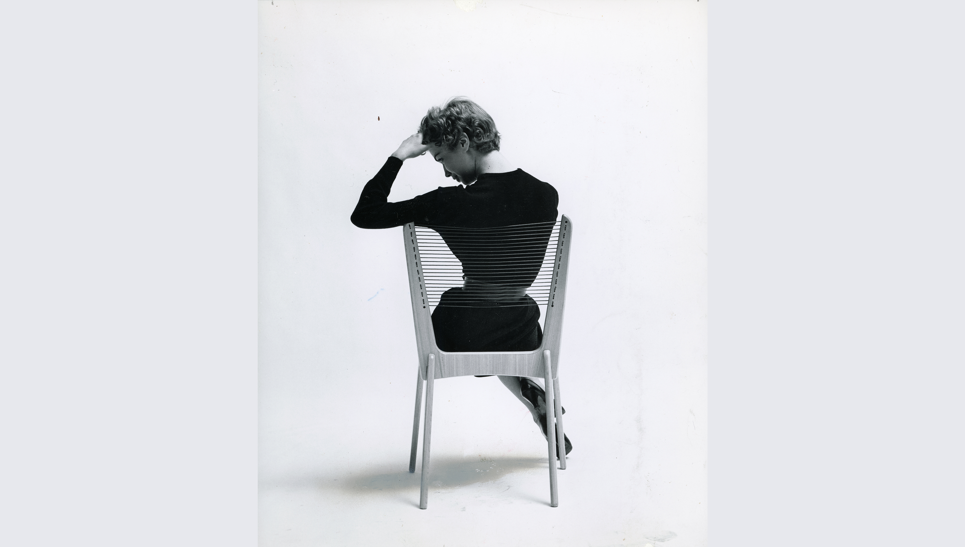 A woman seated on a chair, facing away from the camera, with her back visible in the image.