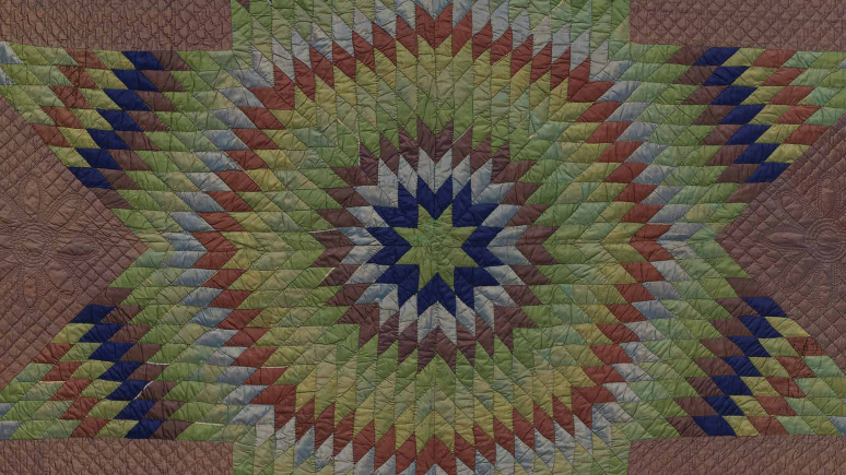 A star-shaped quilt with a striking green, blue, and red pattern, emphasizing its quilted texture and artistic design.