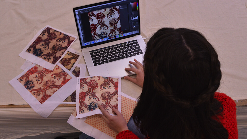 Une jeune femme est assise devant un ordinateur portable entouré de carrés de tissu à motifs.
