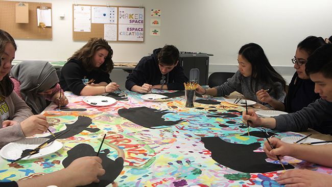 A group of Youth Cabinet members paint at a table onto canvas.
