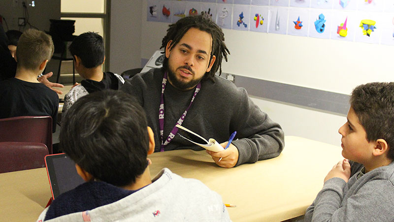 ROM intern talking with two elementary school students at a table
