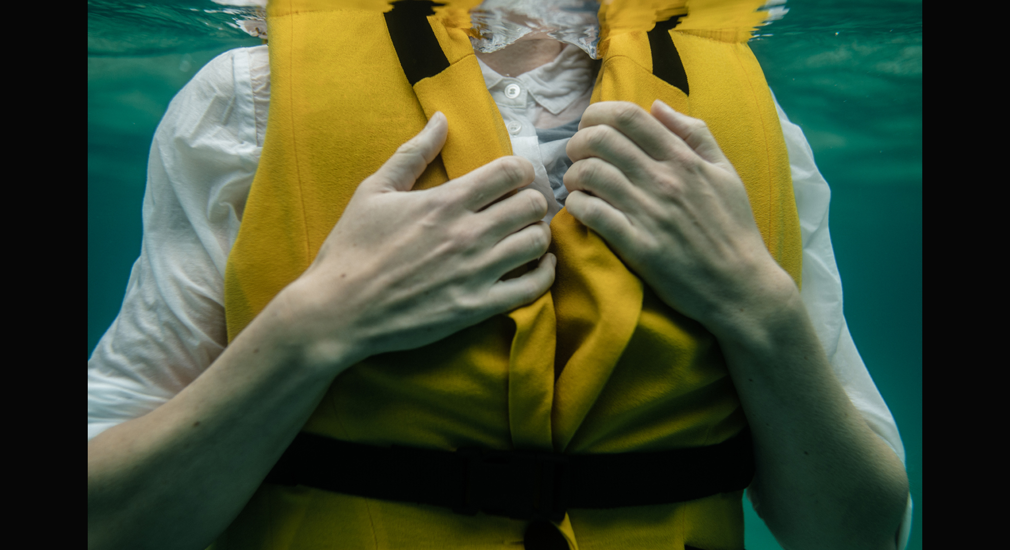 Image taken underwater of a woman's torso fited in a white shirt and yellow lifejacket.
