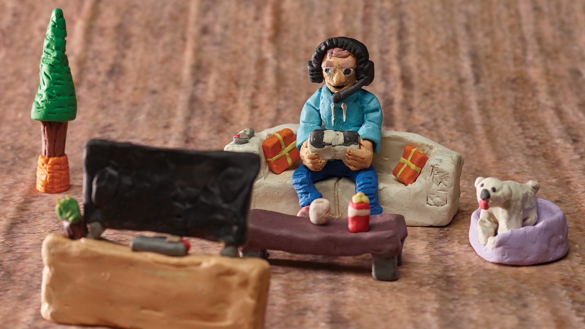 Detail of a diorama showing a person wearing headphones on a couch, playing a video game while looking at a television screen.