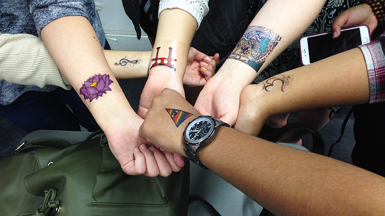 Six students show off their tattoo designs on their arms
