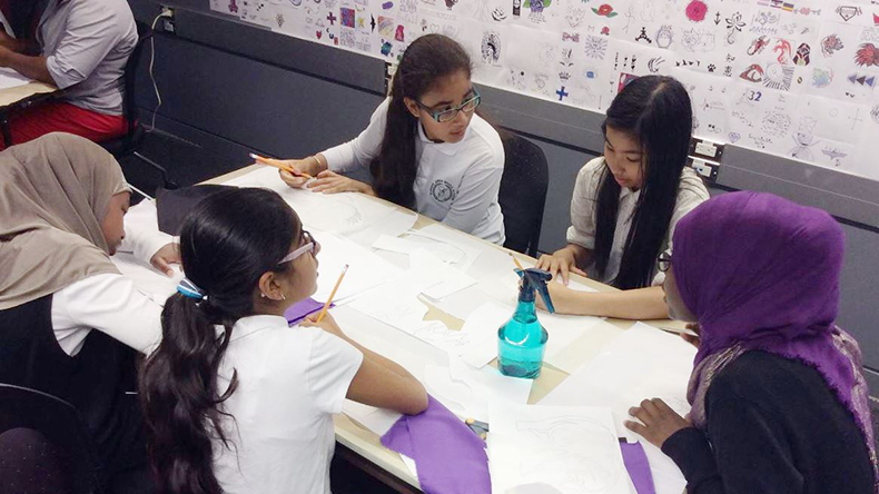 Five students around a table trace flag applique designs onto fusible interfacing fabric
