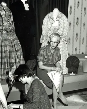 Black and white photo of Dorothy Burnham mounting a costume in the museum.
