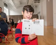 A boy excitedly holds an open activity book showing his stamps and stickers.