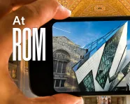 A hand holds a phone whose screen displays an image of the Royal Ontario Museum. At ROM is written next to the phone