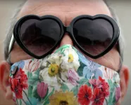 Woman wearing heart-shaped sunglasses and floral face mask.
