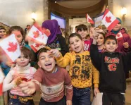 A group of Syrian children smile and wave Canadian flags in front of the ROMâs Schad Gallery of Biodiversity
