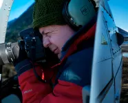 Andrew Wright taking a photograph in a helicopter.
