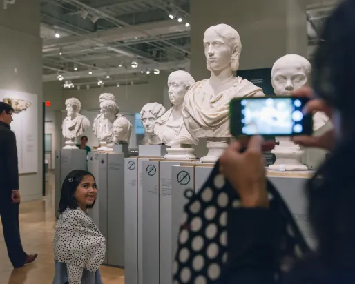 A child posing beside a Roman bust while they are having their photo taken.