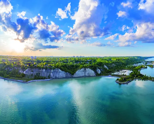 Birdeye view of water an green hills with the sun shining behind clouds