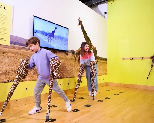 2 children at THEMUSEUM with their hands in giraffe legs