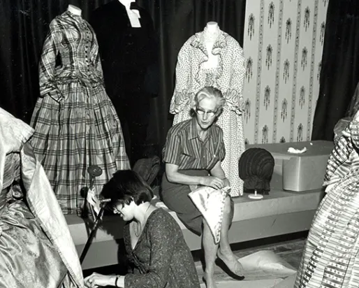 Black and white photo of Dorothy Burnham mounting a costume in the museum.
