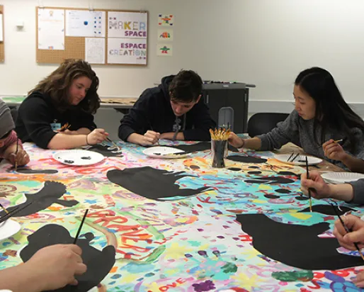 A group of Youth Cabinet members paint at a table onto canvas.
