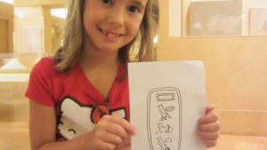 a girl holds a paper showing the name "Charlotte" in hieroglyphs