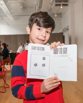 A boy excitedly holds an open activity book showing his stamps and stickers.