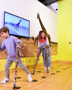 2 children at THEMUSEUM with their hands in giraffe legs