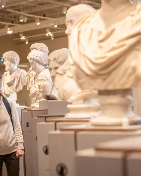 Two visitors look at a row of ancient marble busts on display in a museum gallery.