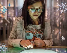 A girl stares down and smiles in wonder as she interacts with a screen in the Museum.