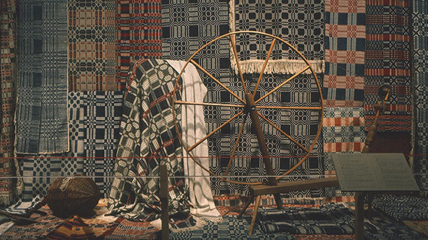 Photograph of <em>Keep Me Warm One Night</em>, the exhibition.
 Photograph of textiles behind a spinning wheel
