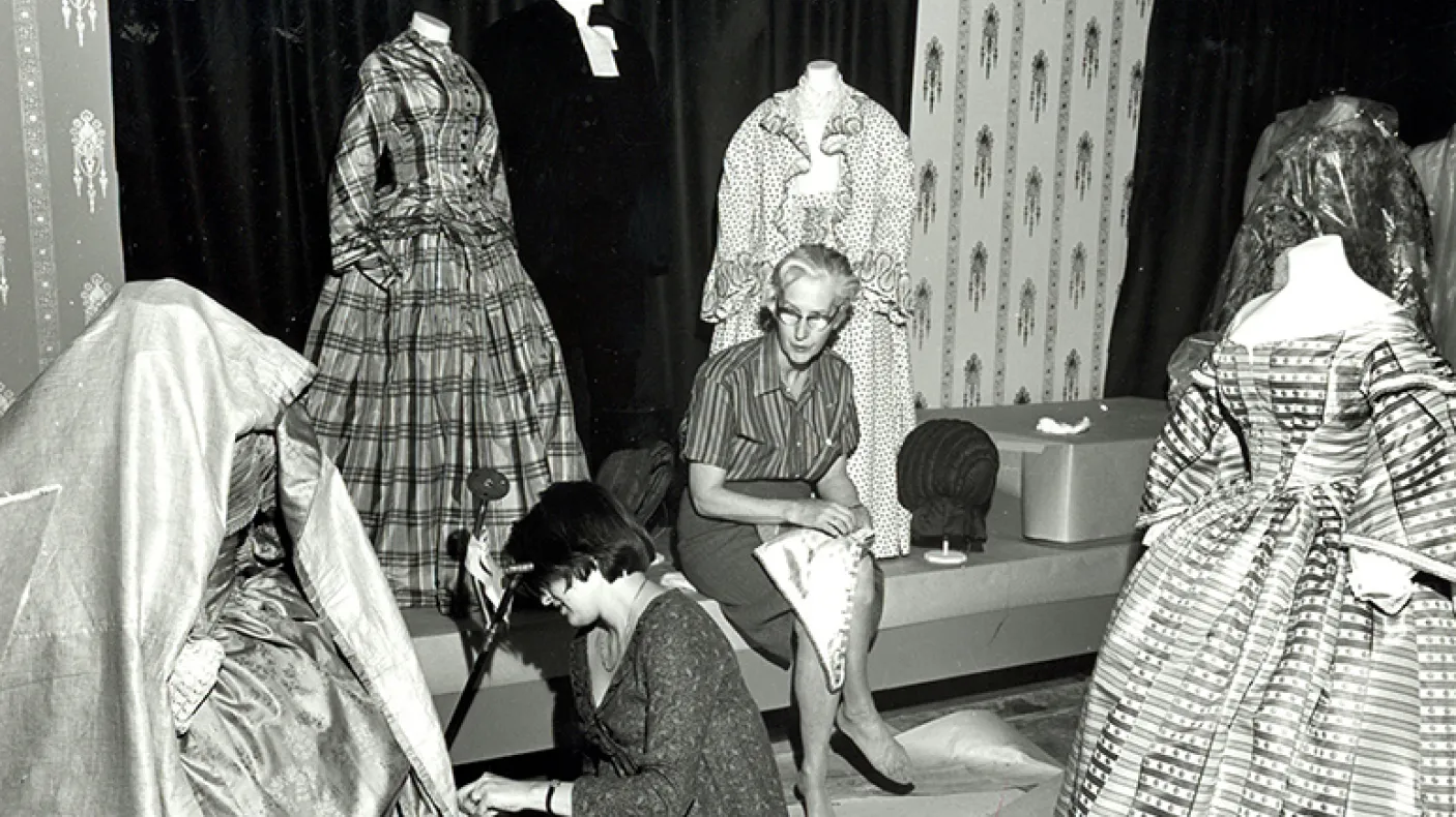 Black and white photo of Dorothy Burnham mounting a costume in the museum.
