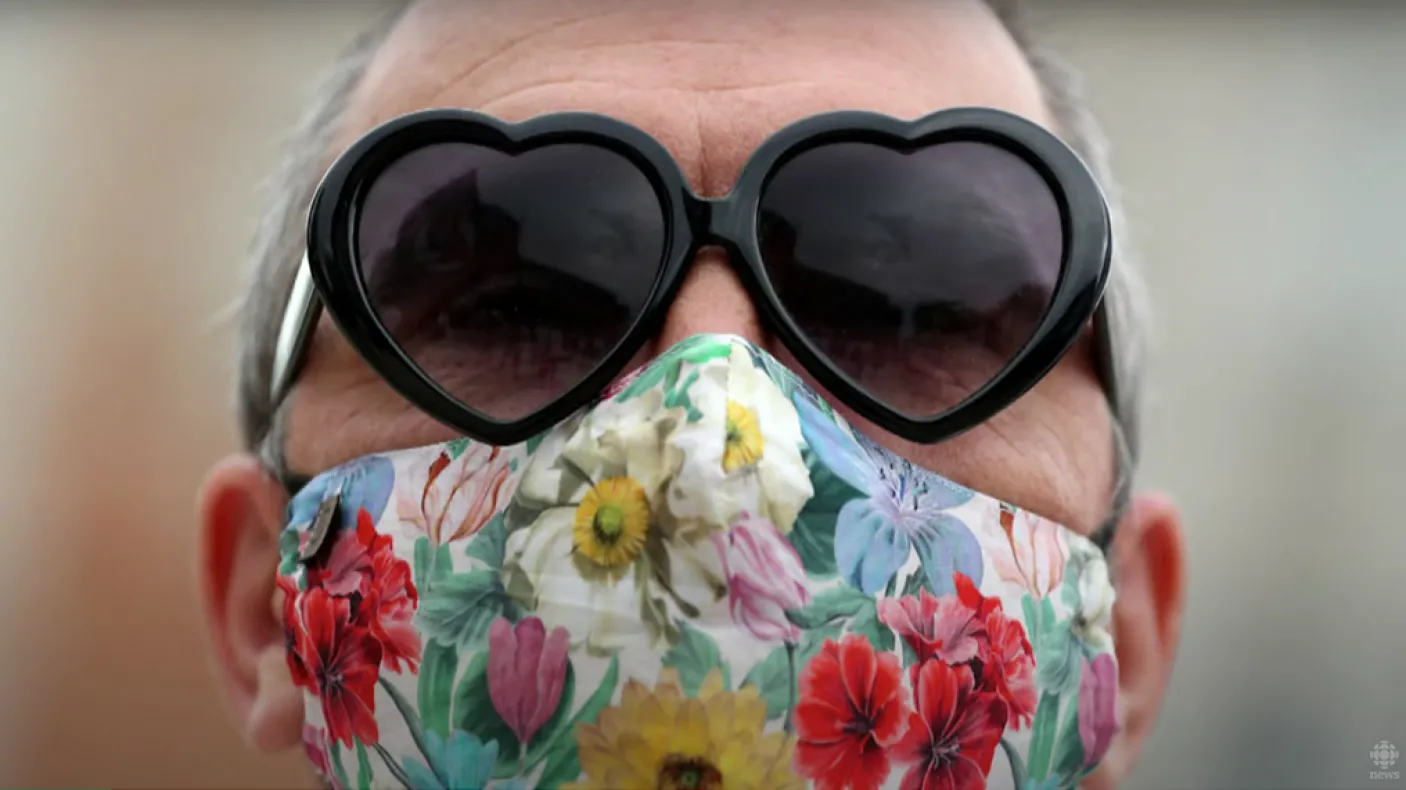 Femme portant des lunettes de soleil en forme de cœur et un masque floral.
