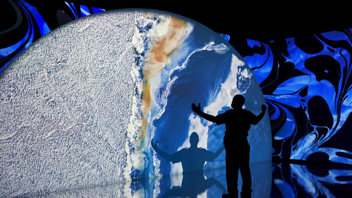 Projection of a planet with a silhouette of a man with his hands in the air looking at a large projection of a planet