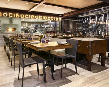 A well-lit dining room. One wall you can see a sign with CIBO, the other wall is glass with a large wine cellar behind