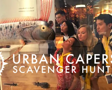 A group on a scavenger hunt pretend to kiss a model of fish behind a glass case