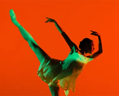 A ballerina, starkly lit in green, dances in front of a red background.