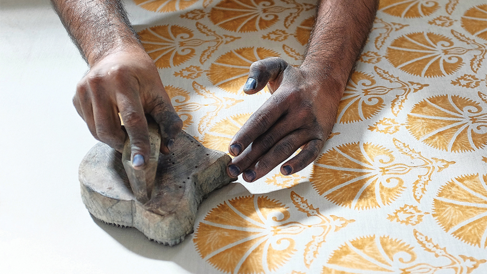 Hands pressing a stamp with yellow paint onto white fabric.