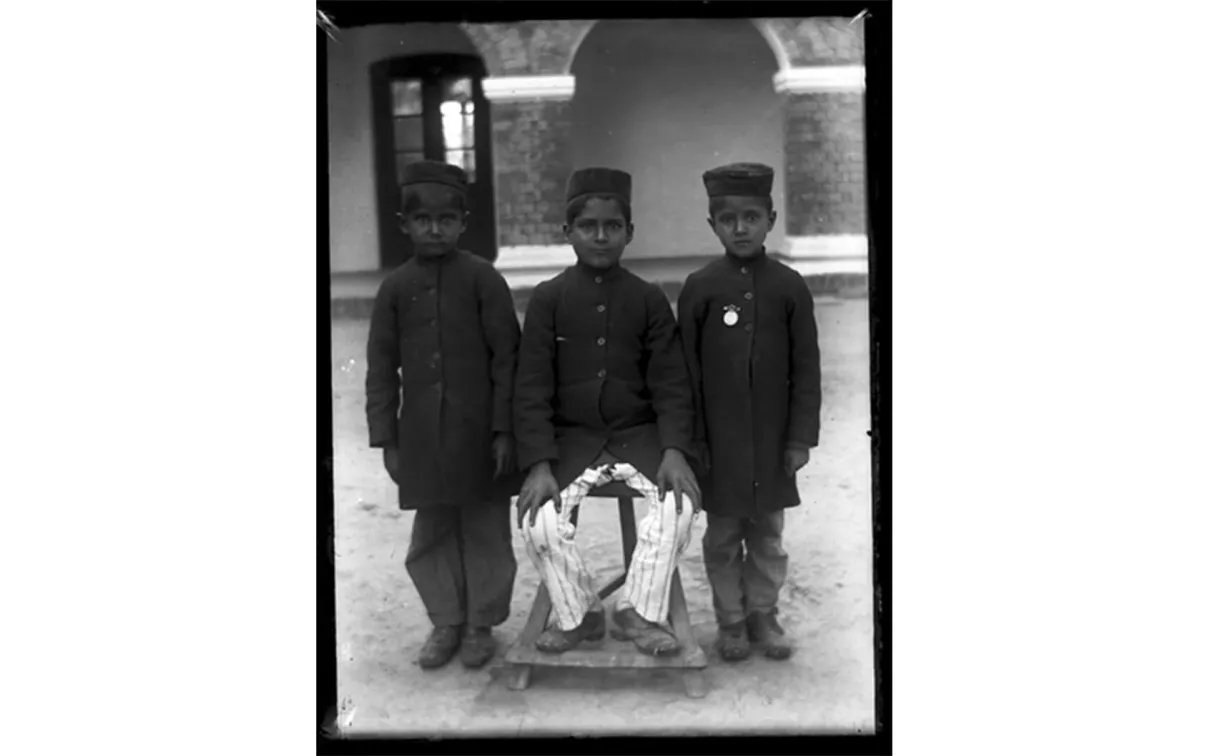 Portrait de trois garçons vêtus de vestes et de chapeaux sombres.