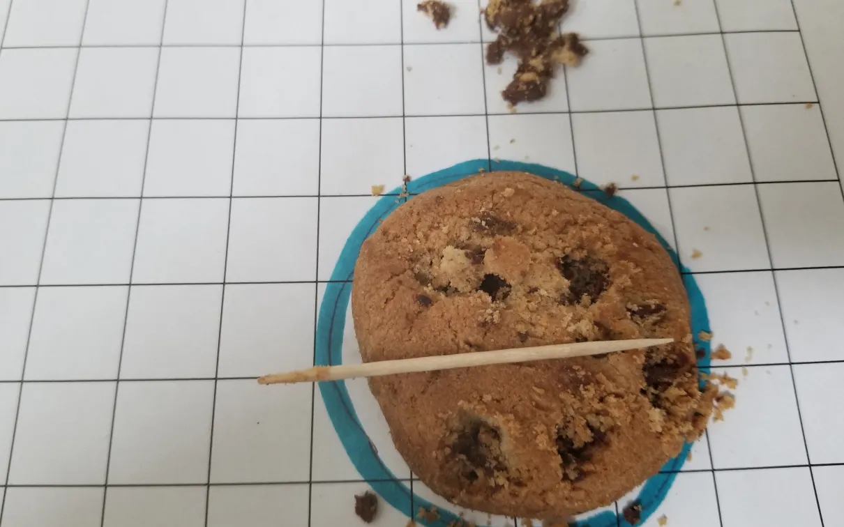 Biscuit aux pépites de chocolat sur papier quadrillé, quelques pépites de chocolat retirées ou "minées" du produit situé à côté.
