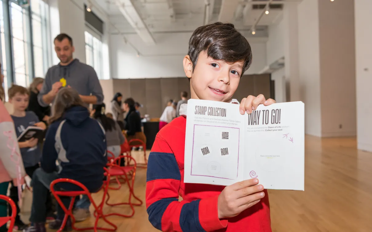 A boy excitedly holds an open activity book showing his stamps and stickers.