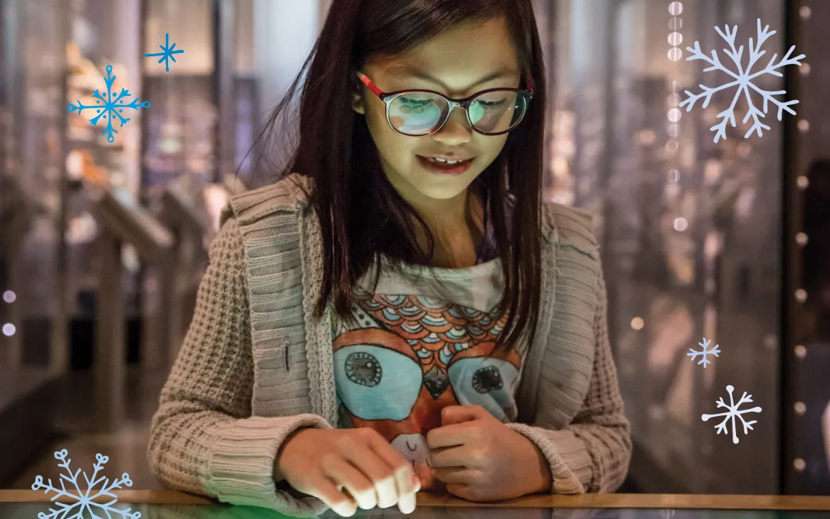 Une jeune fille regarde fixement et sourit avec émerveillement en interagissant avec un écran dans le musée.