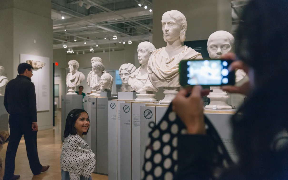 A child posing beside a Roman bust while they are having their photo taken.